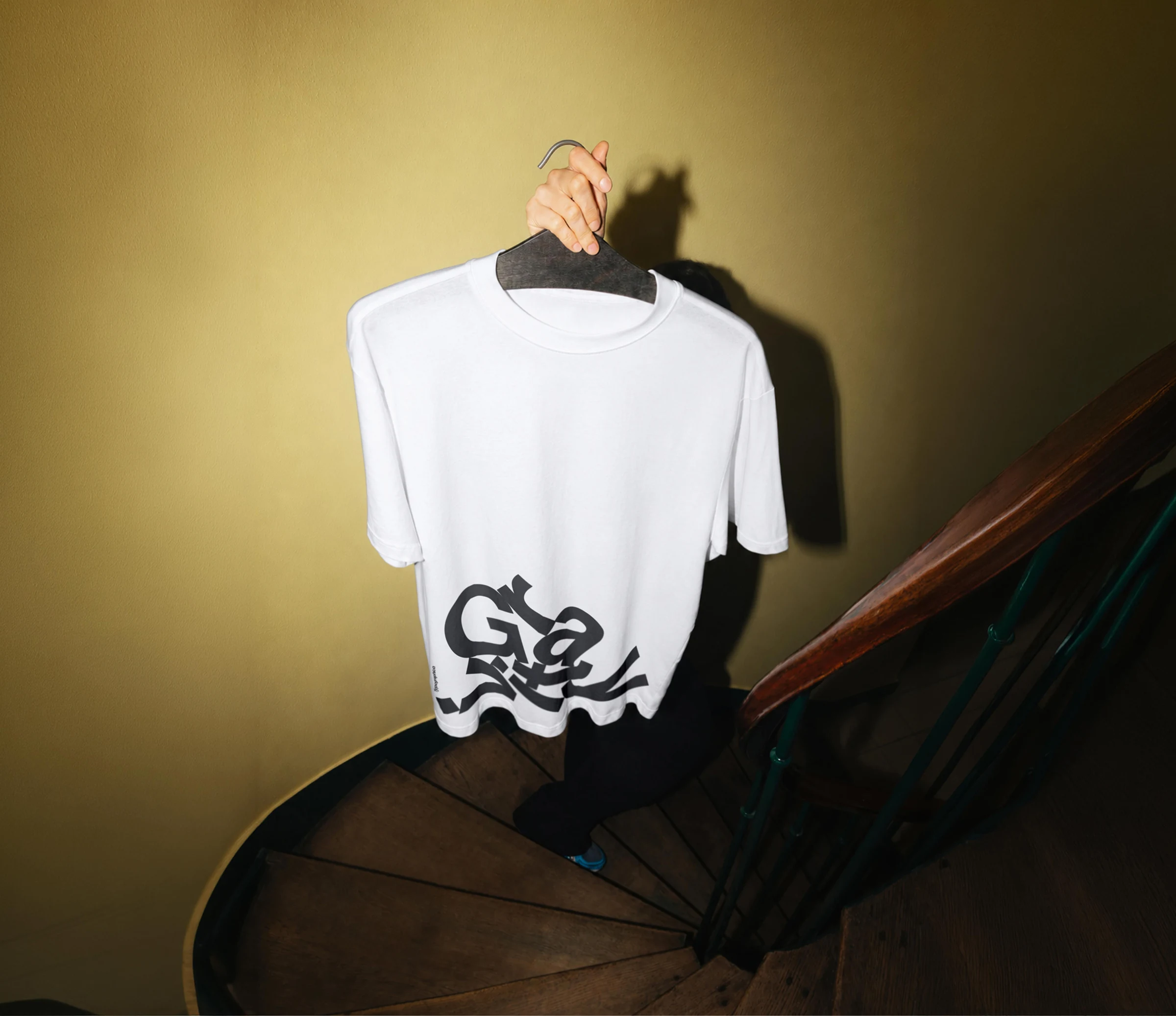 White Gravity T-shirt held on a hanger above a wooden staircase.