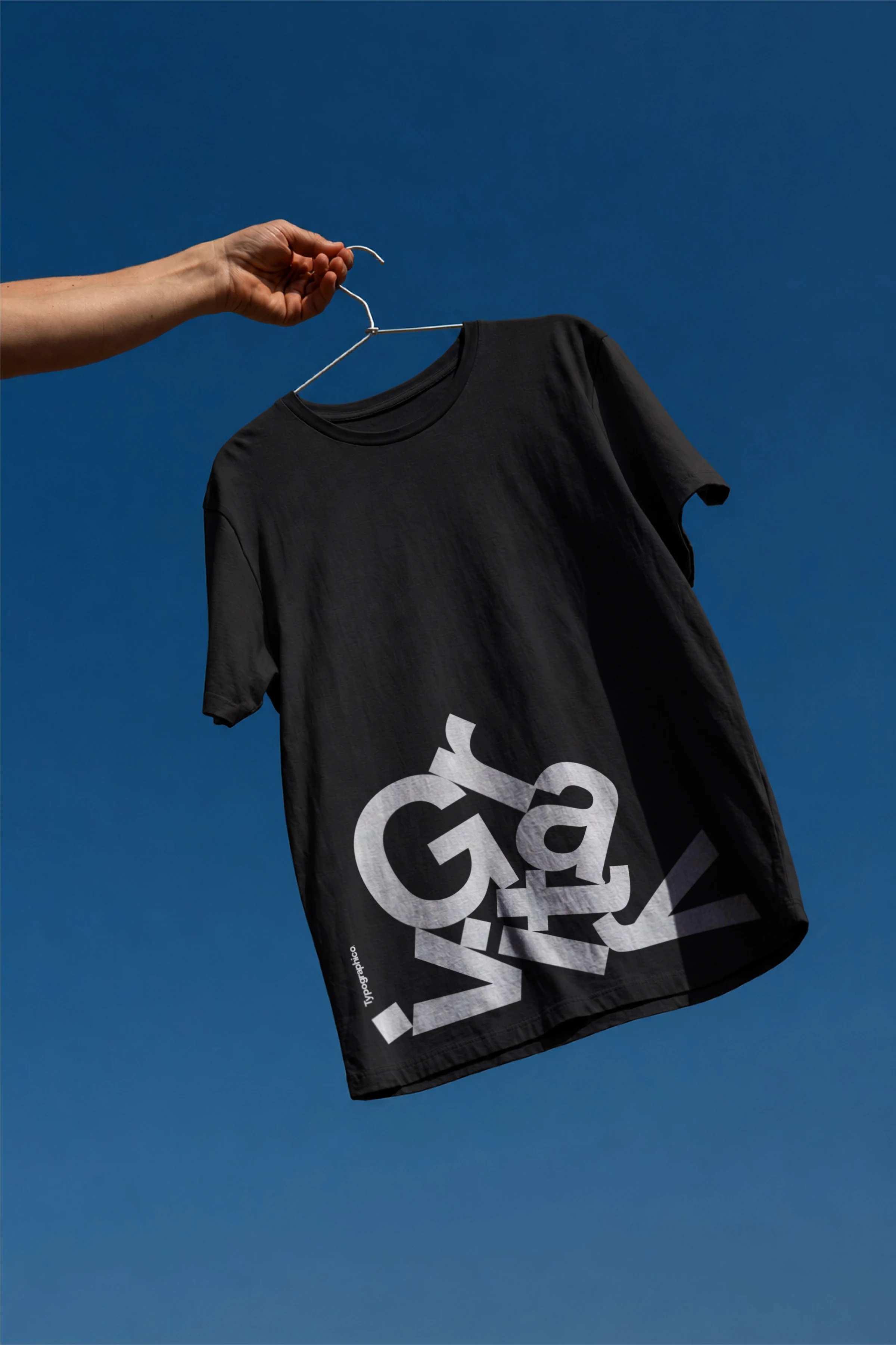 Black T-shirt with the Gravity letter composition, hanging against a blue background.