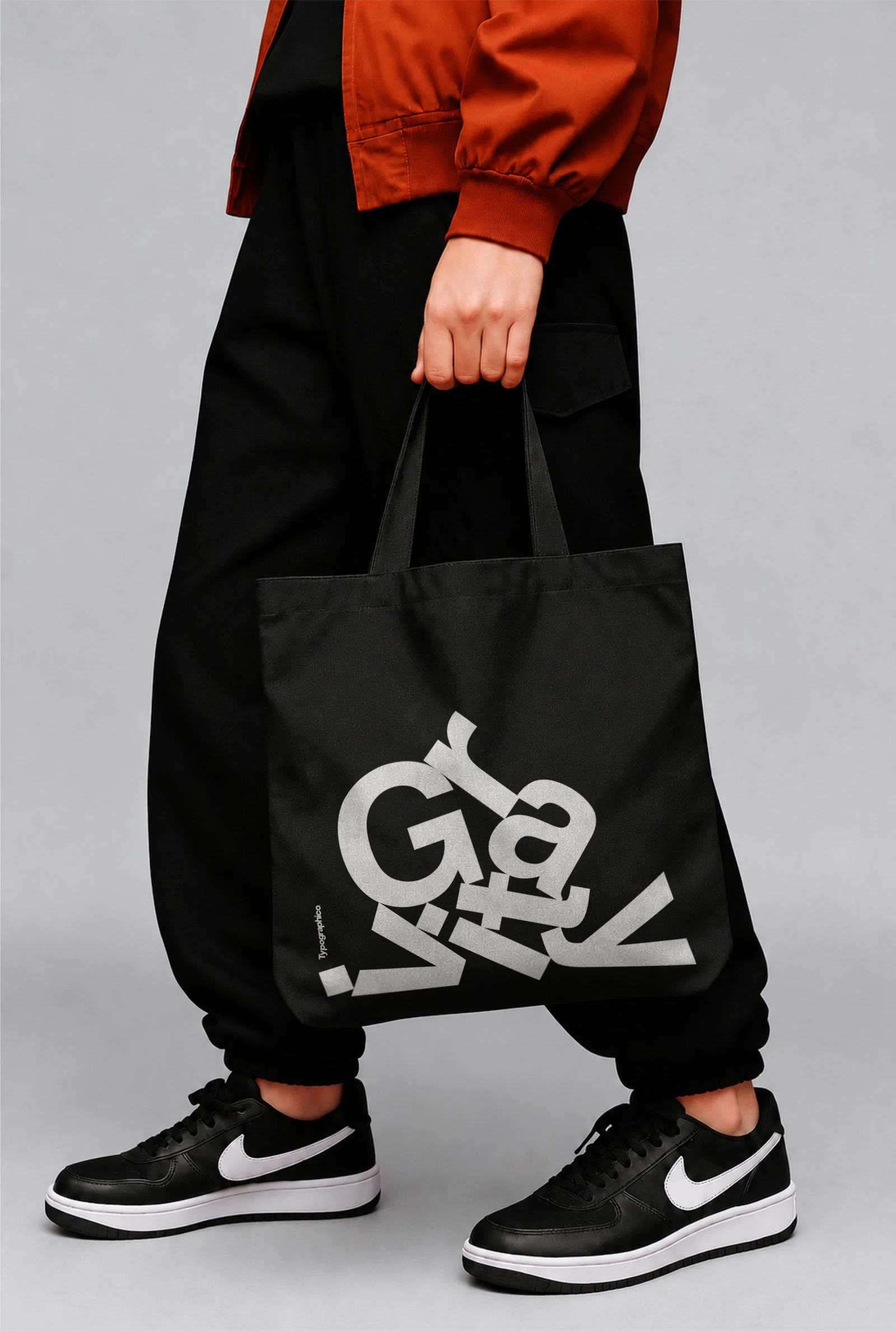 Black Gravity tote bag carried by hand against a light grey background.