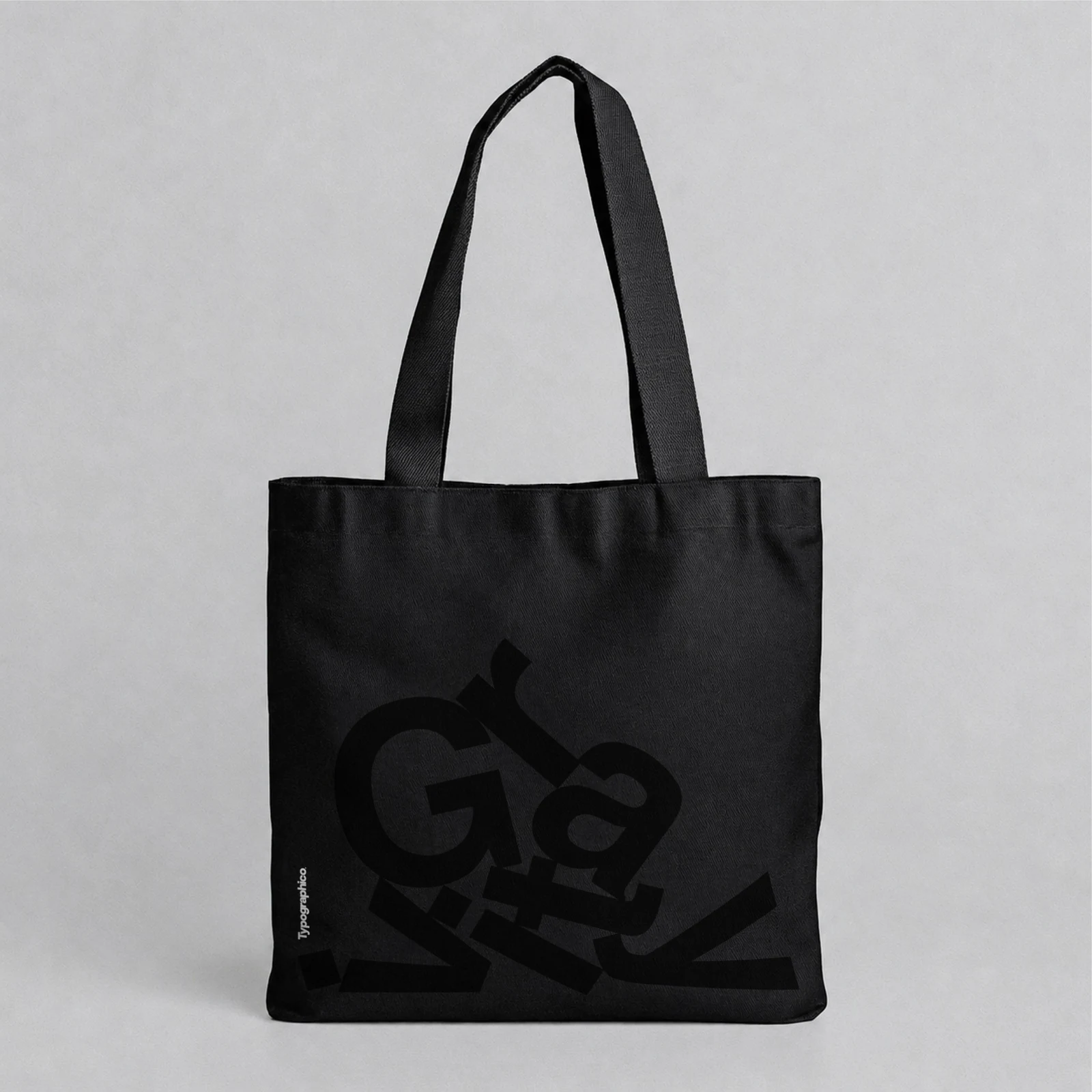 Black tote bag with a tonal black Gravity print on a light grey background.