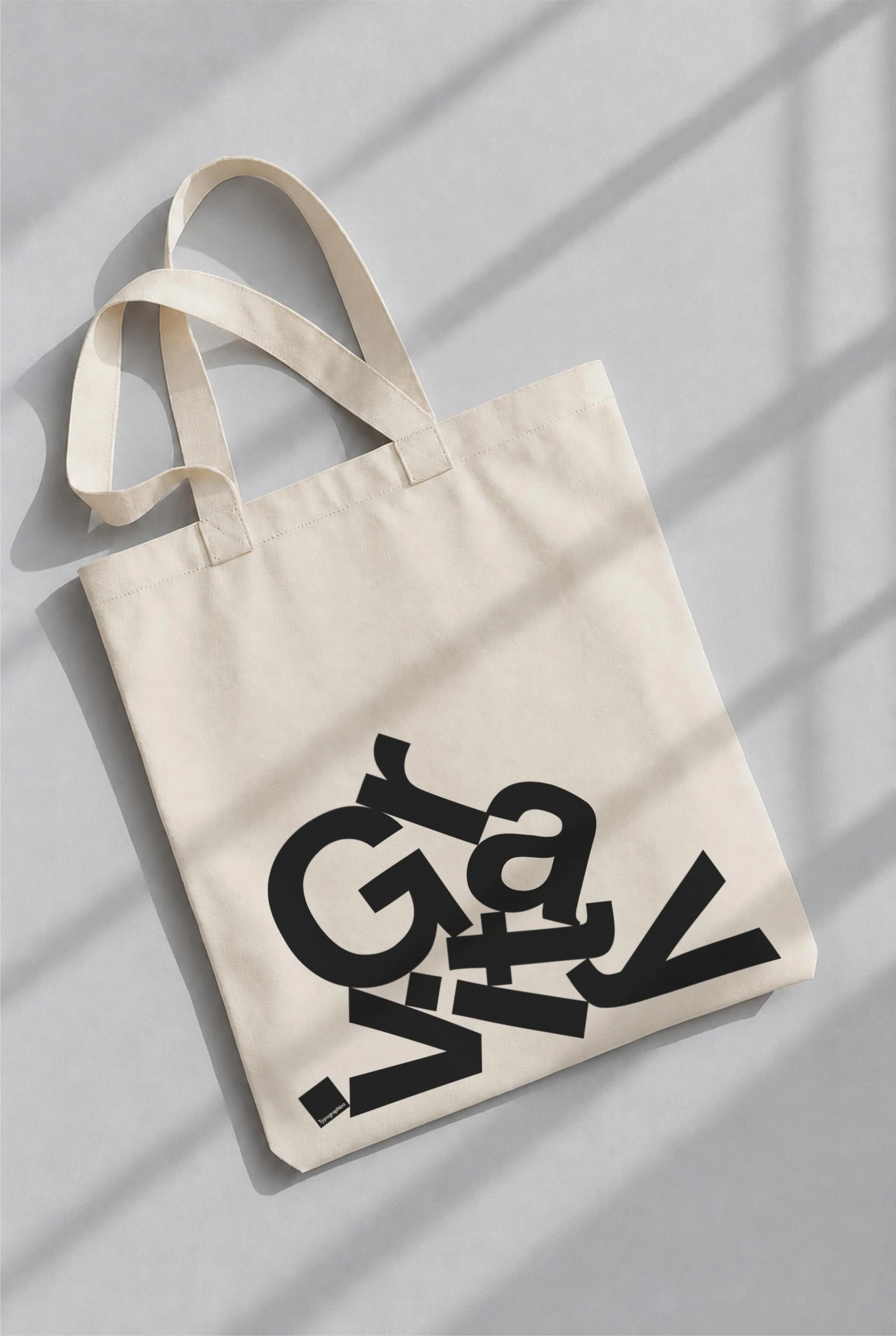White tote bag with a black Gravity print, lying on a softly lit grey surface.
